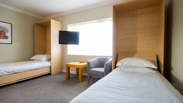 A hotel room with two single beds, a small table, a chair, a television, and a window with curtains.