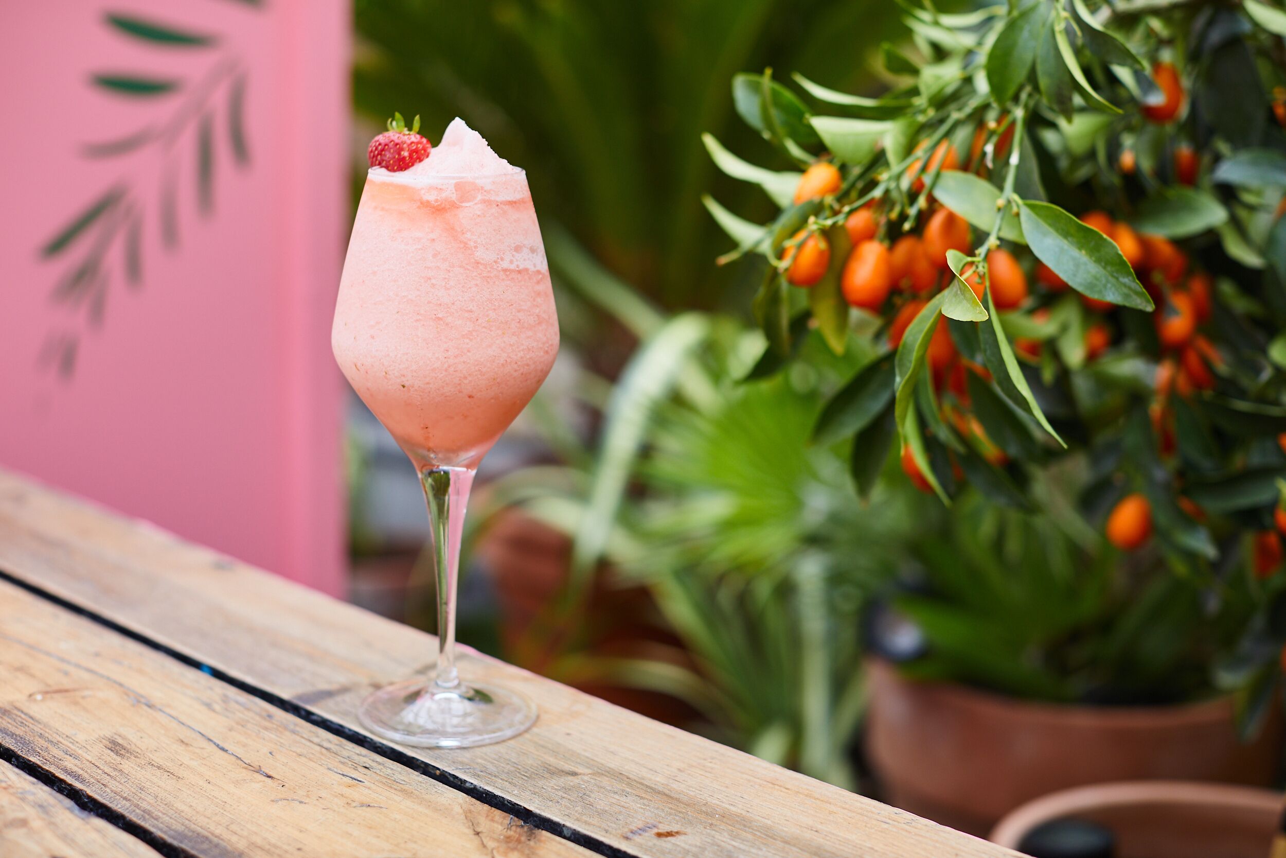 A cocktail glass with a strawberry garnish on a wooden table.