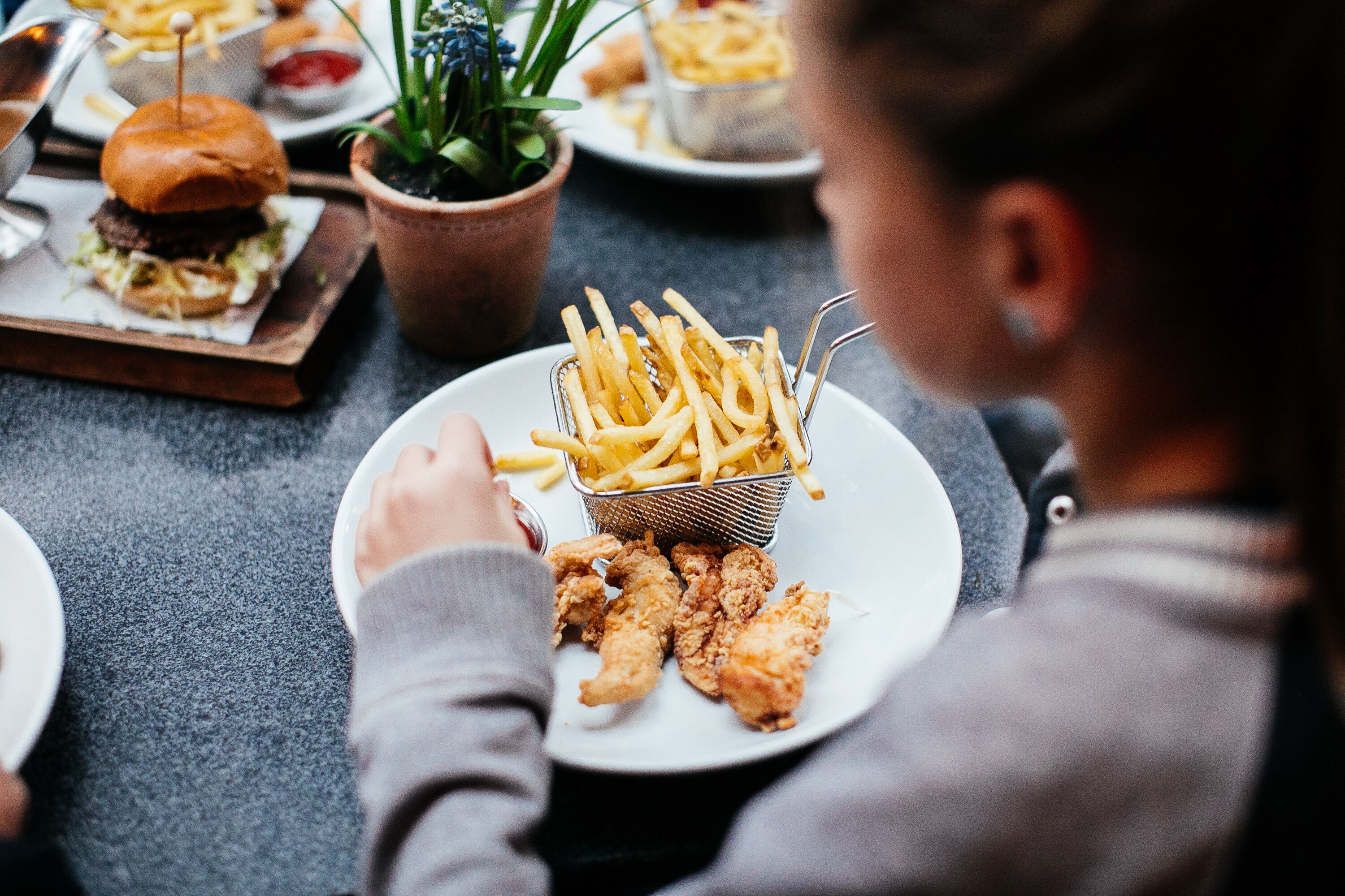 A dining table with a plate of fried chicken and French fries, a burger, and a small plant.