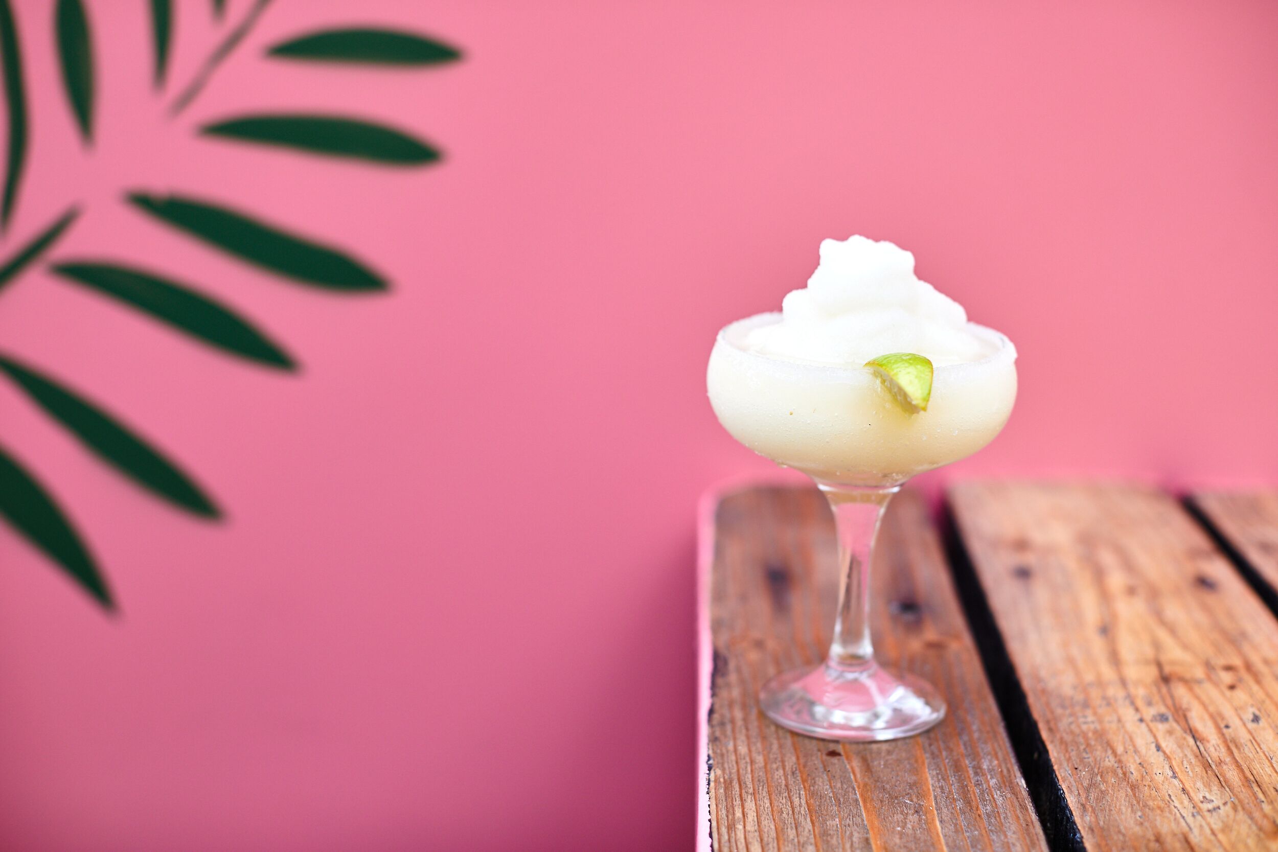 A dessert in a glass on a wooden surface with a pink background.