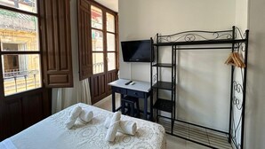 Una habitación de hotel con cama, escritorio, televisión y balcón con puertas de madera.