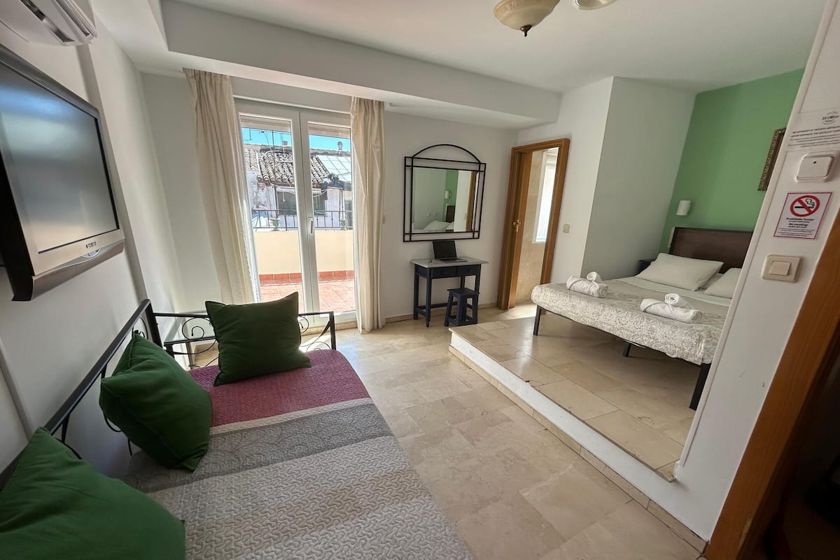 A hotel room with a bed, a desk, a TV, and a balcony with a view of buildings.