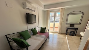 Un dormitorio con cama, televisión, escritorio y balcón.
