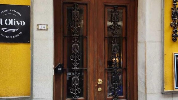 Entrada de hotel con una puerta doble de madera, un escalón que la precede y un cartel con el nombre y la ubicación del hotel.