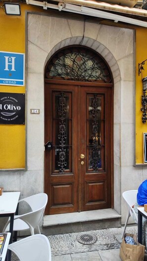 A hotel entrance with a double wooden door, a small step leading up to it, and a sign indicating the hotel name and location. - Hostal El Olivo (Granada)