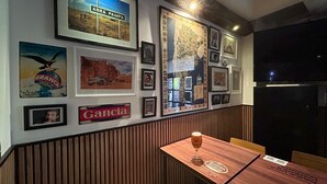 Un interior de restaurante con una mesa con banqueta de madera, cuadros en la pared y un vaso de cerveza sobre la mesa.