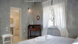 A bedroom with a bed, a bedside table, a chair, and a window with curtains. - Katikies Manis (West Mani)