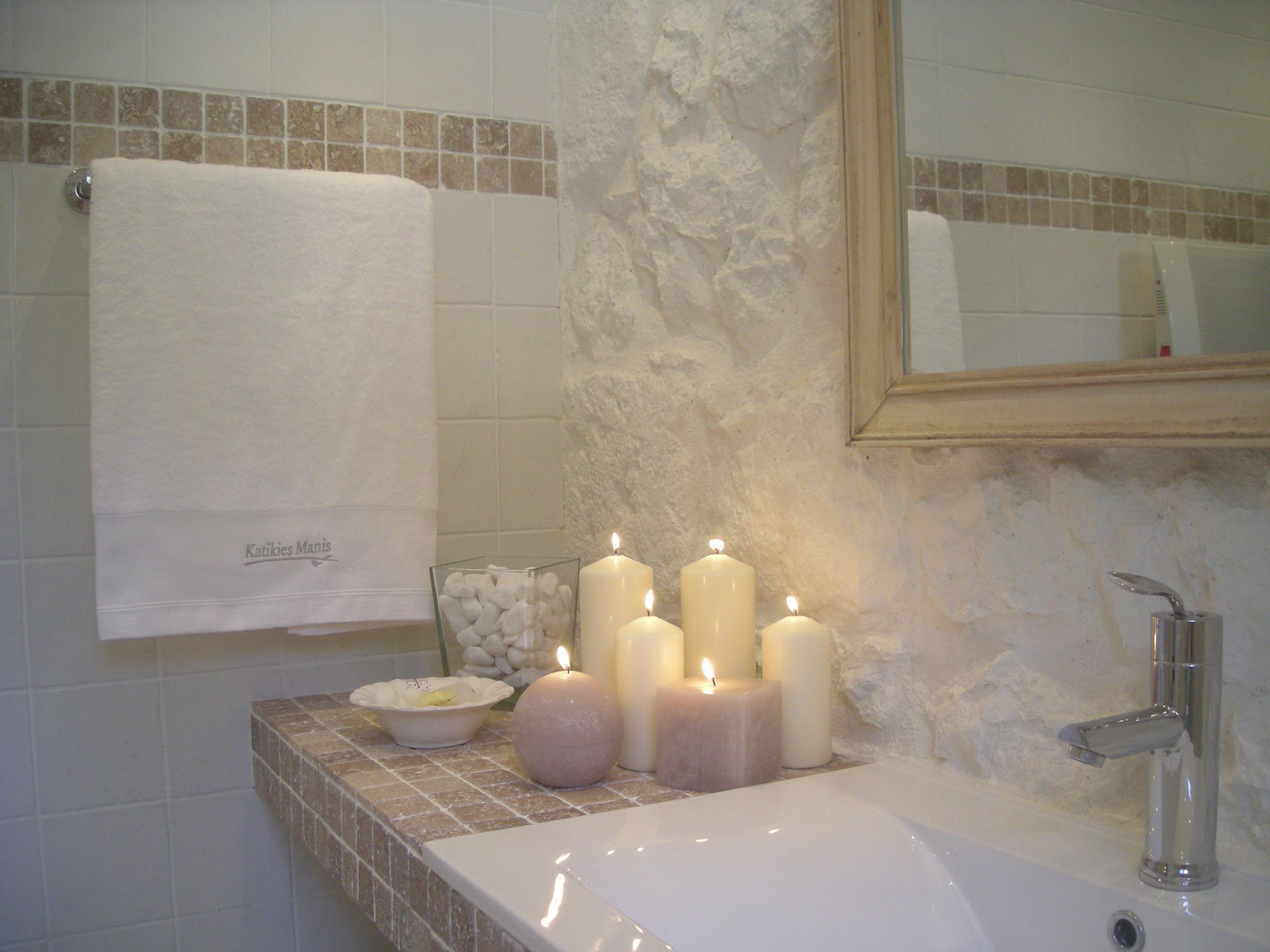 A bathroom with a white sink, multiple candles, a bowl of pebbles, and a towel hanging on the wall.