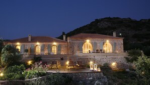A stone building with arched windows and a red-tiled roof, surrounded by greenery and a pool area. - Katikies Manis (West Mani)
