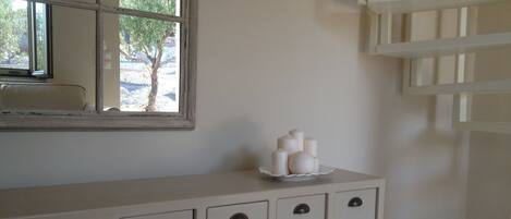 Un baño con tocador blanco, espejo y ventana con vista a árboles.