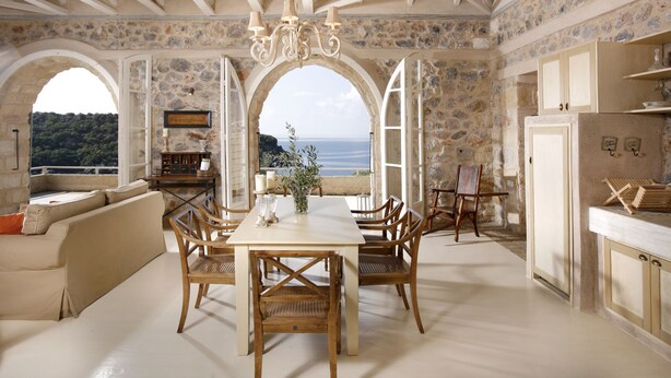 A spacious dining area with a table and chairs, a chandelier, and a view of the sea through large windows. - Katikies Manis (West Mani)