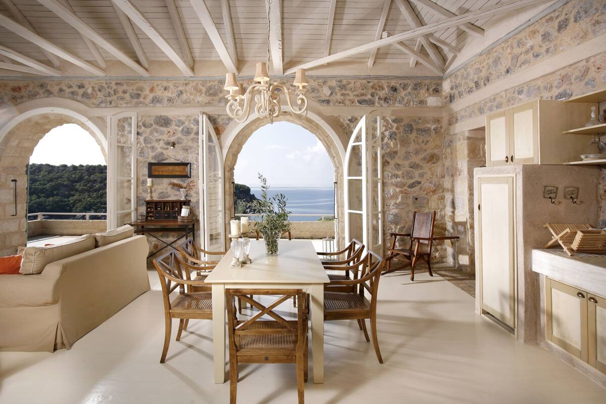 A spacious dining area with a table and chairs, a chandelier, and a view of the sea through large windows.
