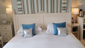 Una habitación de hotel con una cama grande, dos almohadas, una mesita de noche, una lámpara y un panel decorativo en la pared.