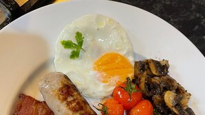 Un plato con comida para el desayuno, incluyendo huevos, salchichas, tomates, champiñones, tocino y frijoles.