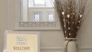 Un monitor de computadora con un letrero que dice 'Bath House Welcome', un florero con ramas decorativas y un teclado sobre un escritorio.