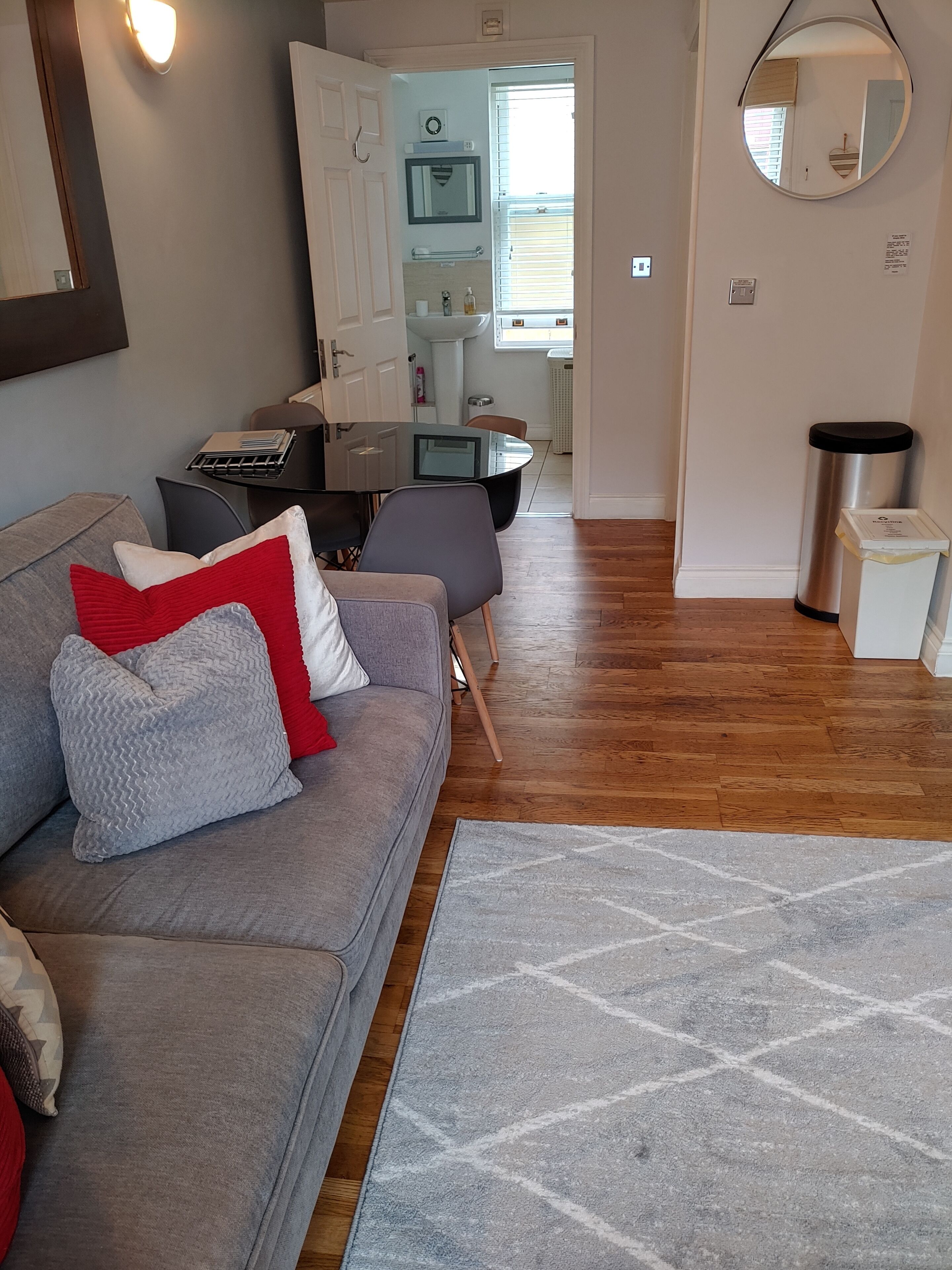 Un salon avec un canapé gris, des coussins rouges et gris, une petite table avec un ordinateur portable et un tapis gris.
