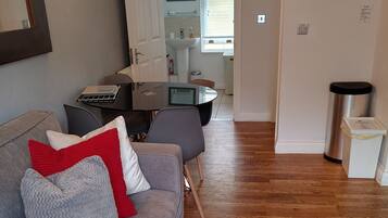 Un salon avec un canapé gris, des coussins rouges et gris, une petite table avec un ordinateur portable et un tapis gris.