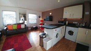 Um espaço habitacional compacto com sofá, tapete vermelho, máquina de lavar, micro-ondas e televisão.