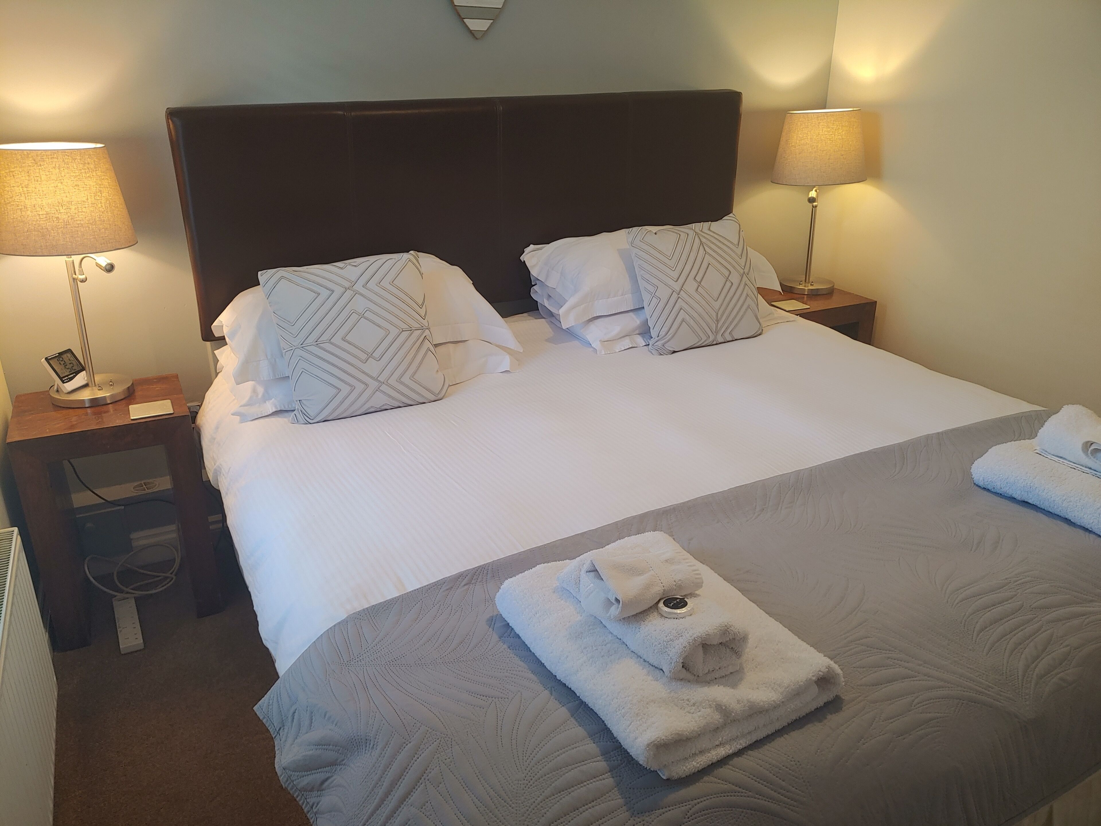 Un lit bien fait, avec deux oreillers, une table de chevet avec une lampe et une serviette pliée posée sur le lit.