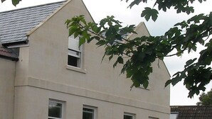 Um edifício de dois andares com fachada simétrica, várias janelas e um galho de árvore em primeiro plano.