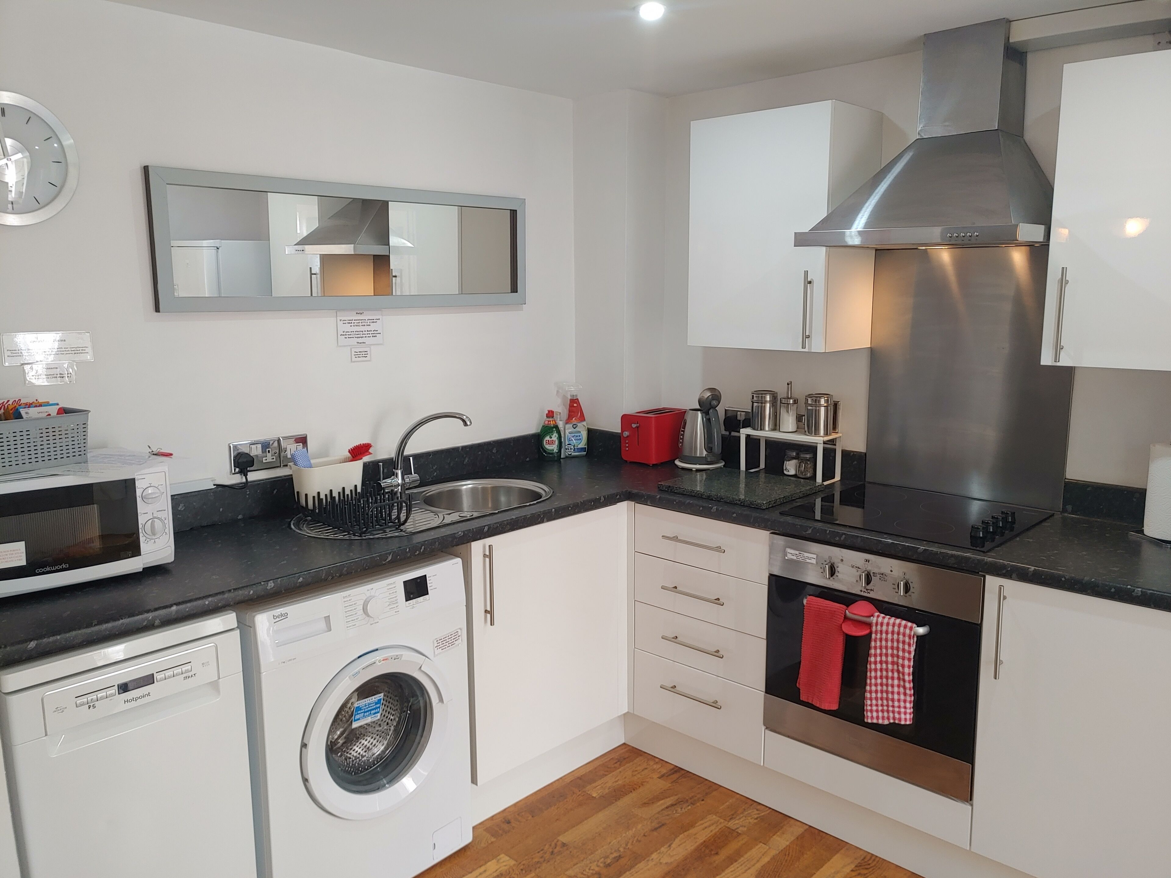 A compact kitchen with a built-in dishwasher, a microwave, a washing machine, a sink, and a stainless steel range hood.