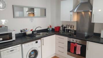 A compact kitchen with a built-in dishwasher, a microwave, a washing machine, a sink, and a stainless steel range hood.