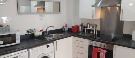 A compact kitchen with a built-in dishwasher, a microwave, a washing machine, a sink, and a stainless steel range hood.