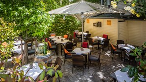 Un espace extérieur aménagé en terrasse, avec plusieurs tables et chaises, entouré de verdure et protégé par un grand parasol.