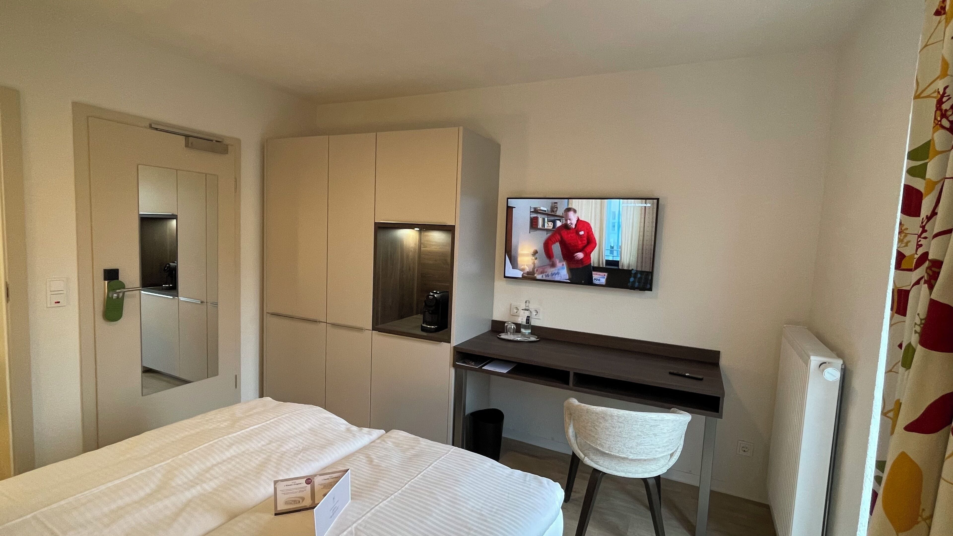 A hotel room with a bed, a desk with a chair, a television, and a mirror.
