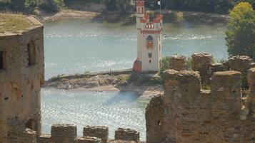 Uma torre de pedra histórica junto a um rio, rodeada por ruínas.
