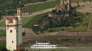 Un castillo en una colina con una torre y un barco en el río.