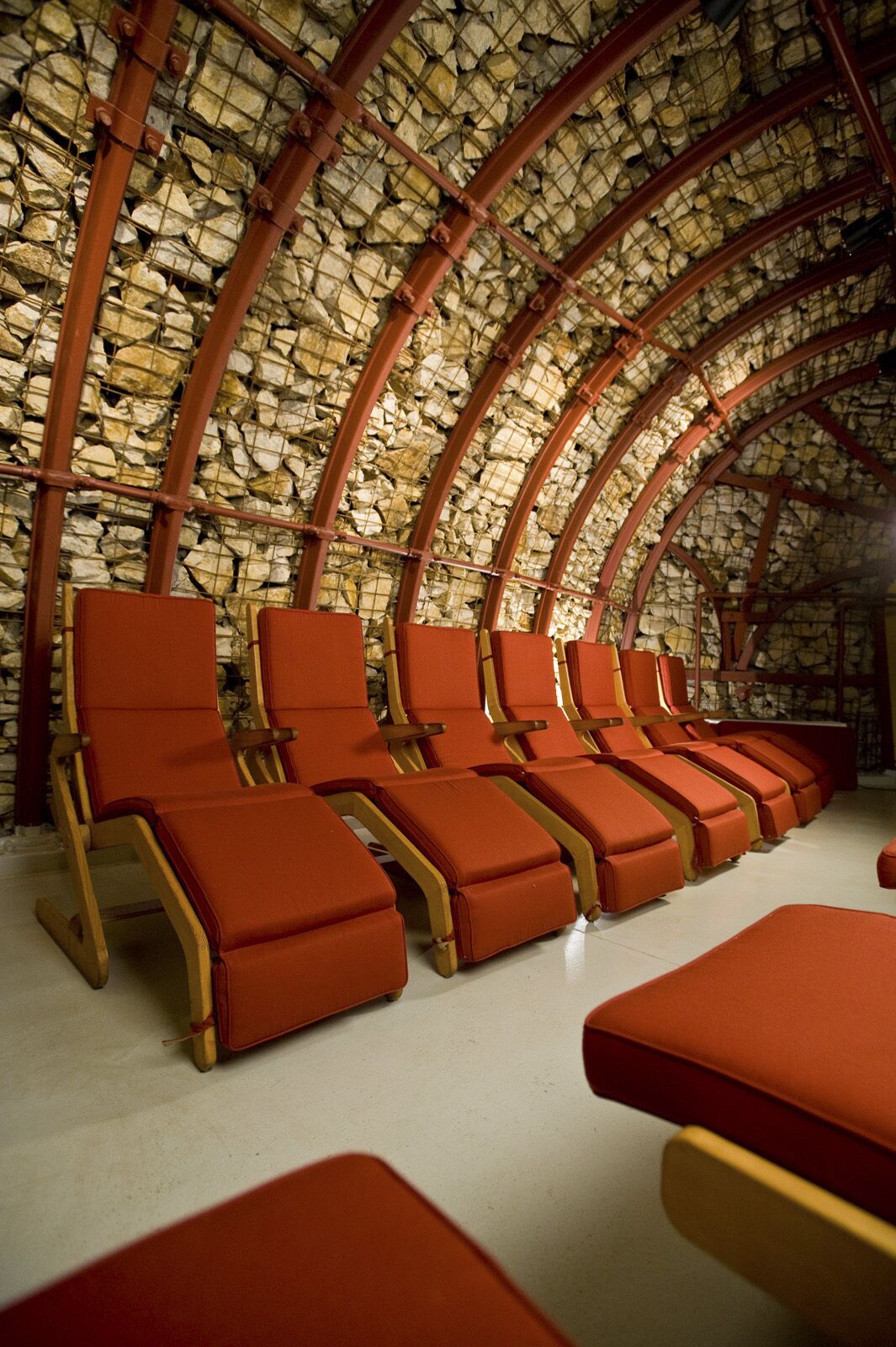 A row of red lounge chairs with a stone wall and arched ceiling.