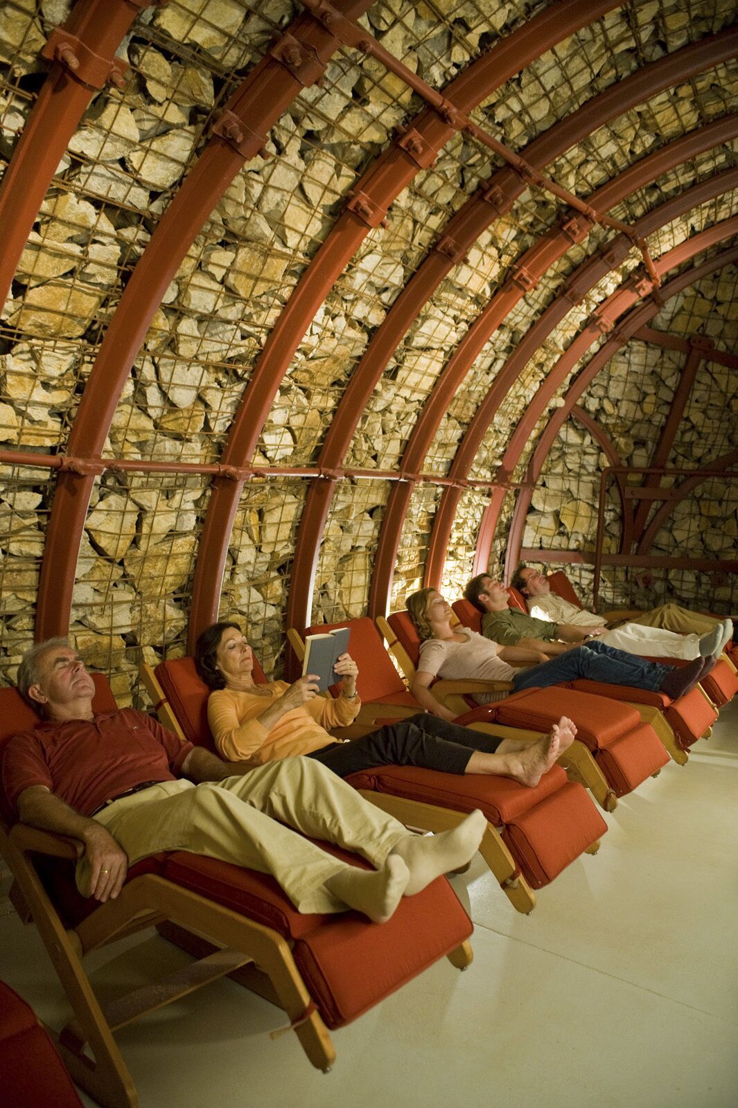 Ein Spa mit Steinsäulen und Holzbalken, mit Liegestühlen und einer Person, die ein Buch liest.