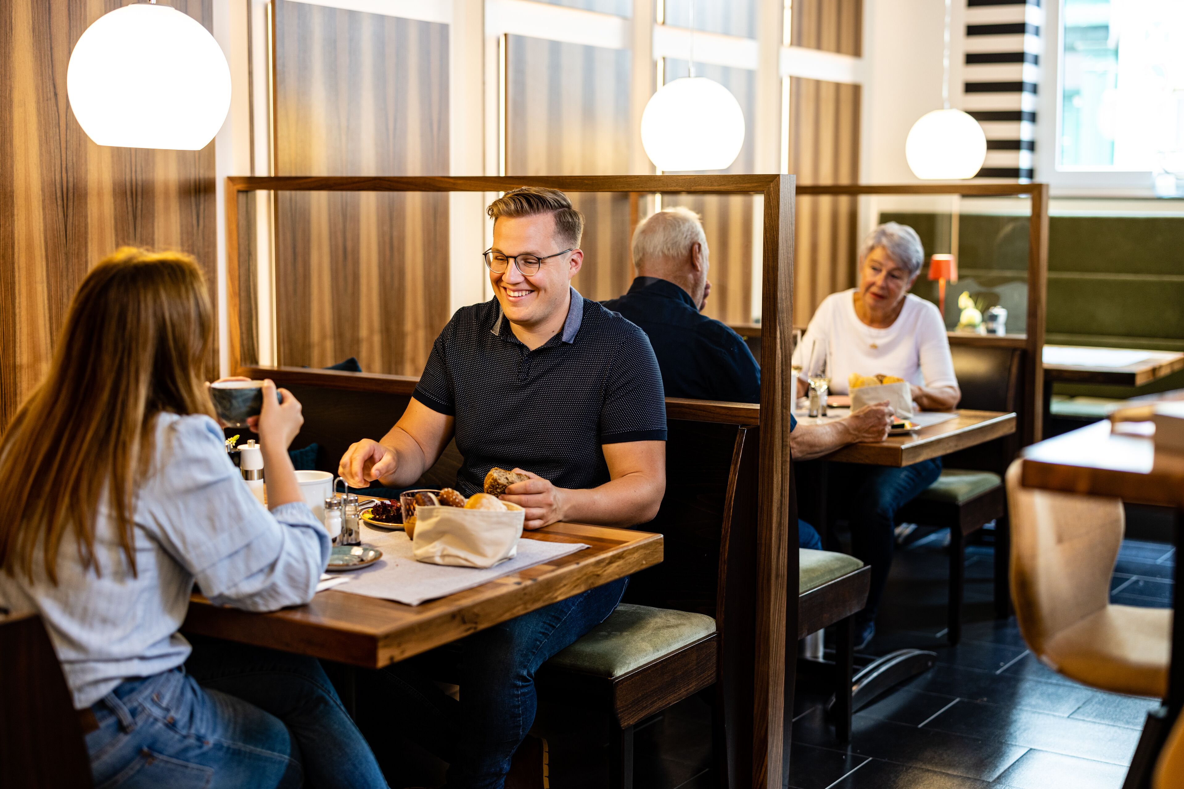 Restaurante com paredes de painel de madeira, cabines individuais e iluminação pendente.