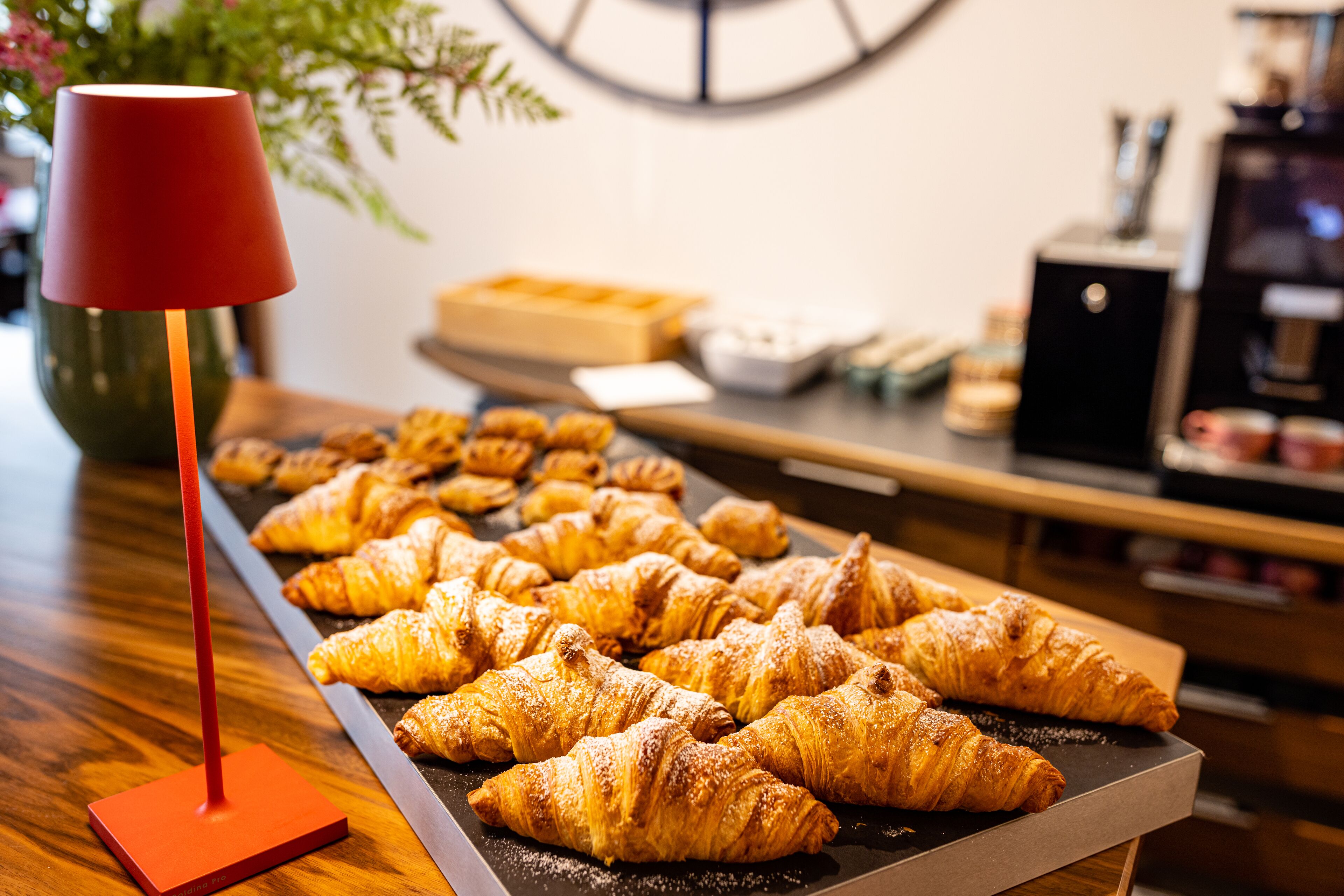 Puisella pöydällä on tarjotin täynnä croissantteja, ja etualalla näkyy punainen lamppu.