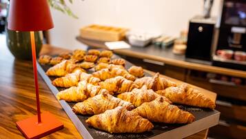 Puisella pöydällä on tarjotin täynnä croissantteja, ja etualalla näkyy punainen lamppu.