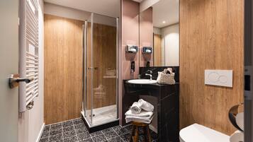 Un baño moderno con cabina de ducha de vidrio, tocador de madera y inodoro blanco.