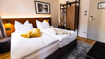 A hotel room with a neatly made bed, a nightstand with a lamp, a coat rack, and a framed picture on the wall.