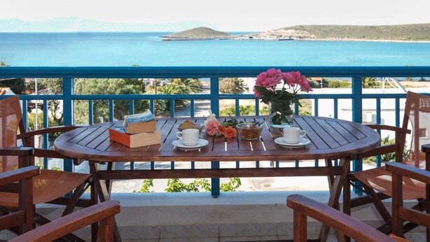 A wooden table with a view of the sea, a flower vase, and a book. - Athena Apartments & Studios (Kithira)