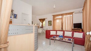 A living room with a red sofa, a coffee table, and a TV. There is a dining area with a table and chairs in the background. - Athena Apartments & Studios (Kithira)