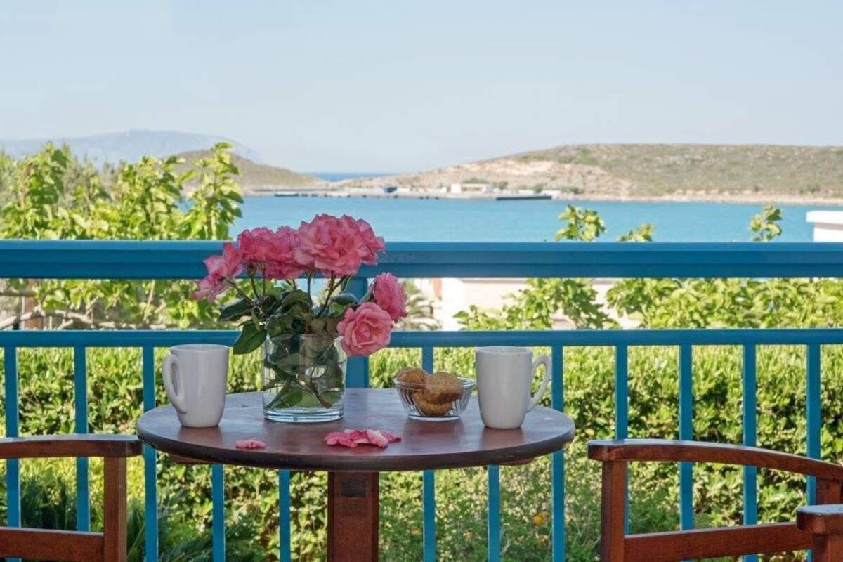 A balcony with a table set for two, featuring a vase of pink flowers, two cups, and a plate with cookies.