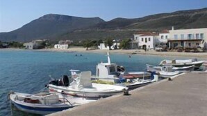 A coastal marina with boats docked, a sandy beach, and buildings in the background. - Athena Apartments & Studios (Kithira)