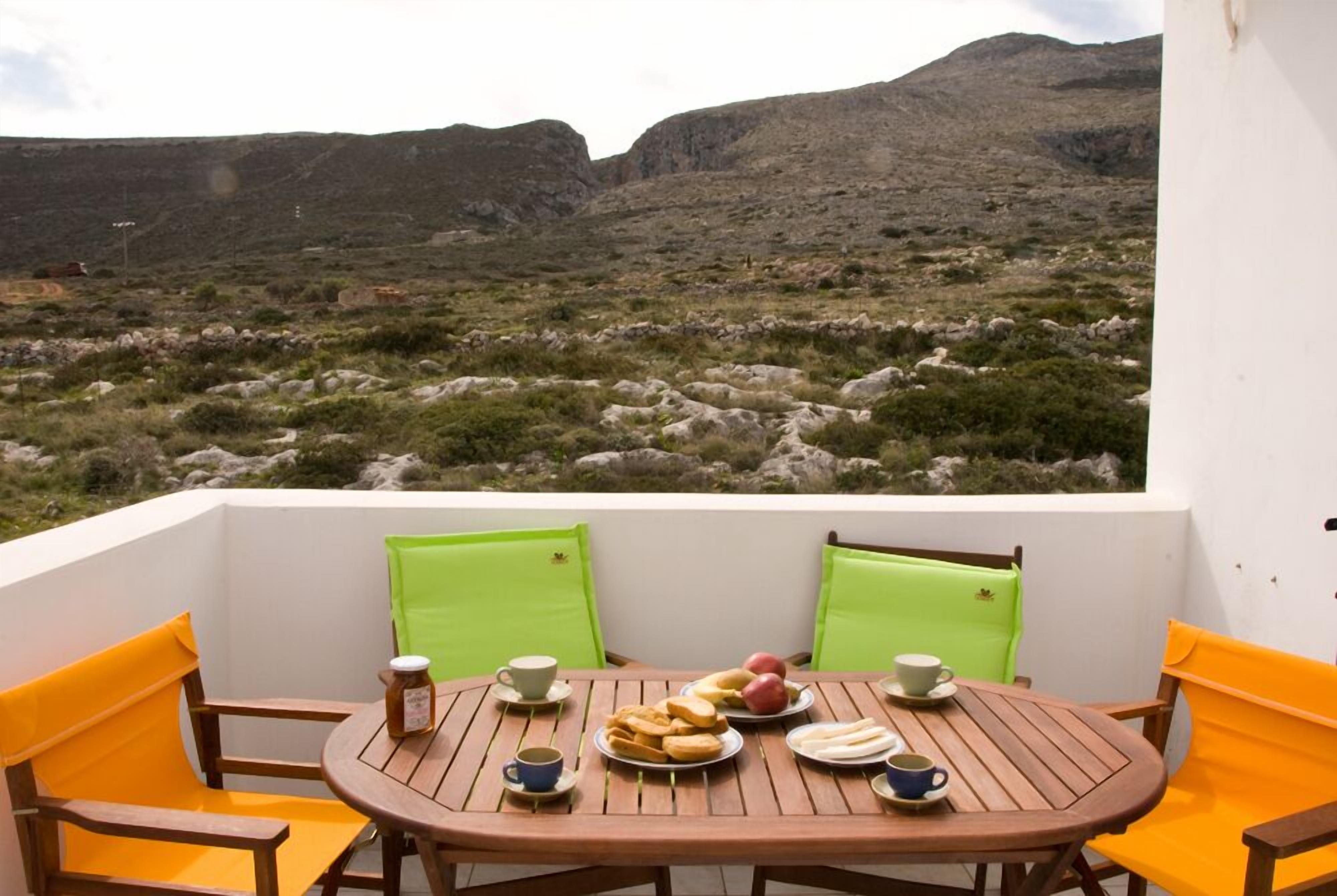 A round wooden table with chairs, a view of rocky terrain, and a white wall.