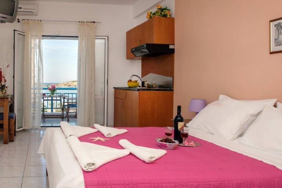 A hotel room with a bed, a small kitchenette, a balcony with a view, and a television.
