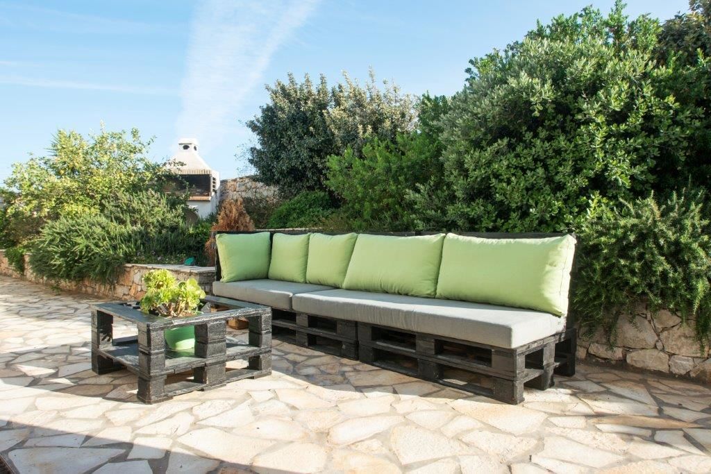 An outdoor seating area with a sofa and a table, surrounded by stone flooring and greenery.