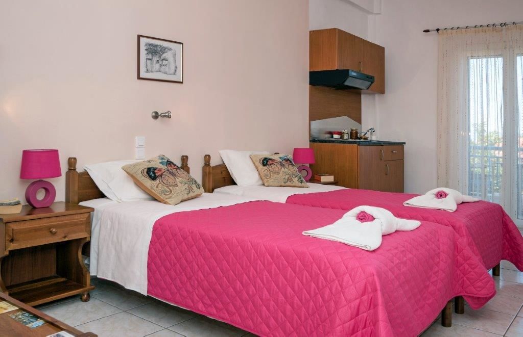 A hotel room with two beds, a small kitchenette, and a window with curtains.
