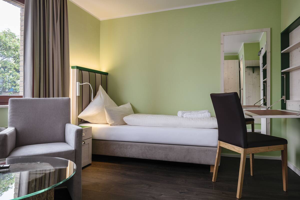 A room with a bed, a chair, a desk, and a mirror.