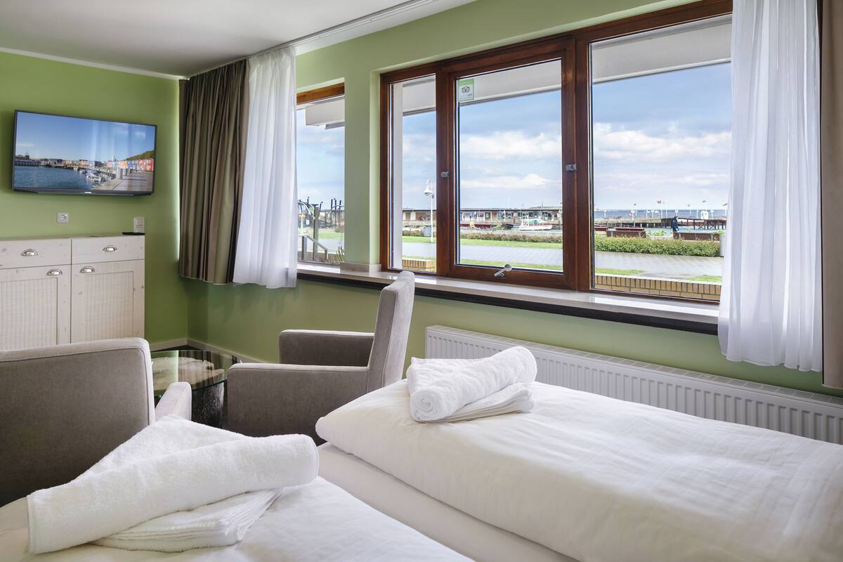 A hotel room with two beds, a TV on the wall, and a view of a harbor.