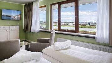 A hotel room with two beds, a TV on the wall, and a view of a harbor.