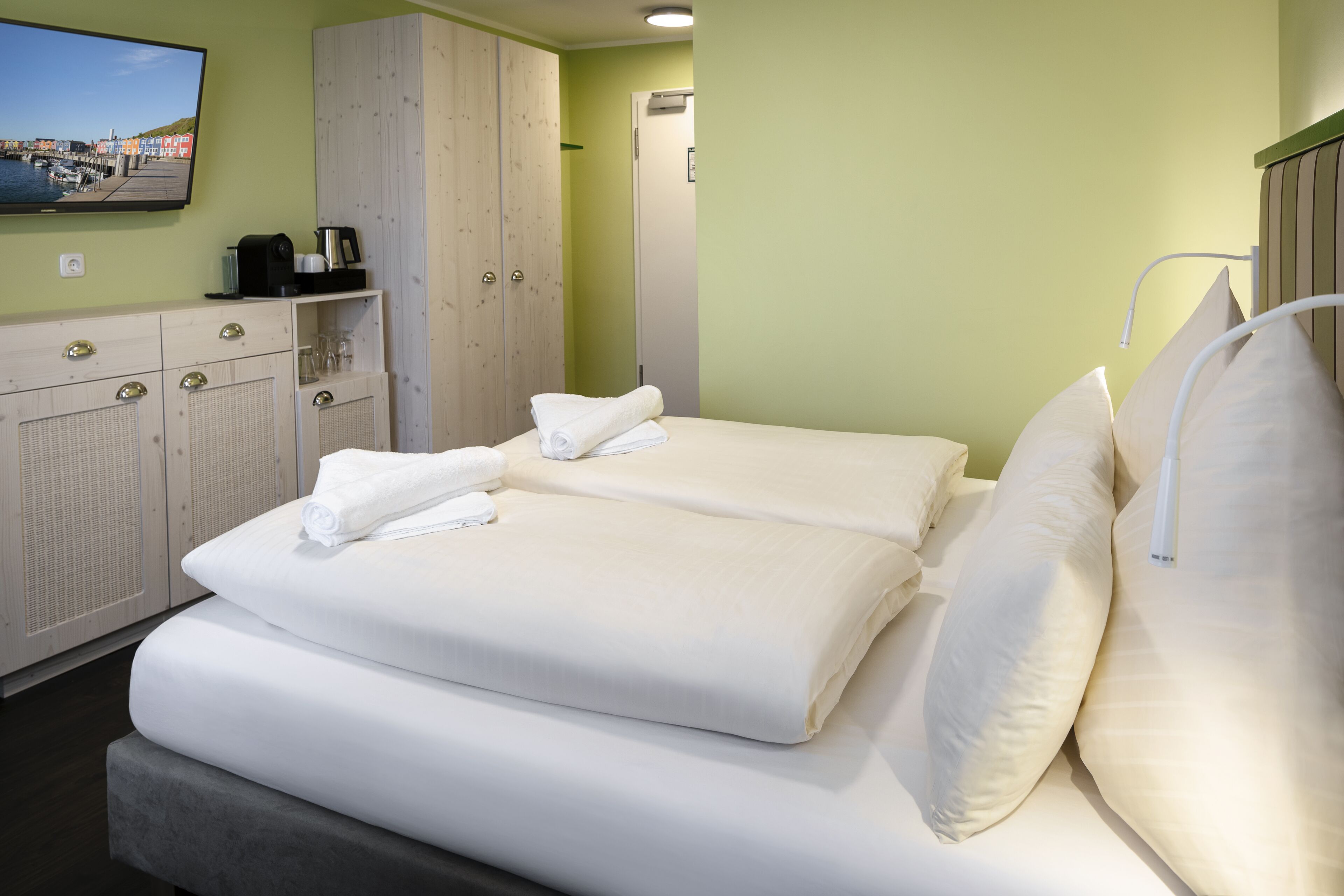 A hotel room with two beds, a wardrobe, a television, and a coffee machine.